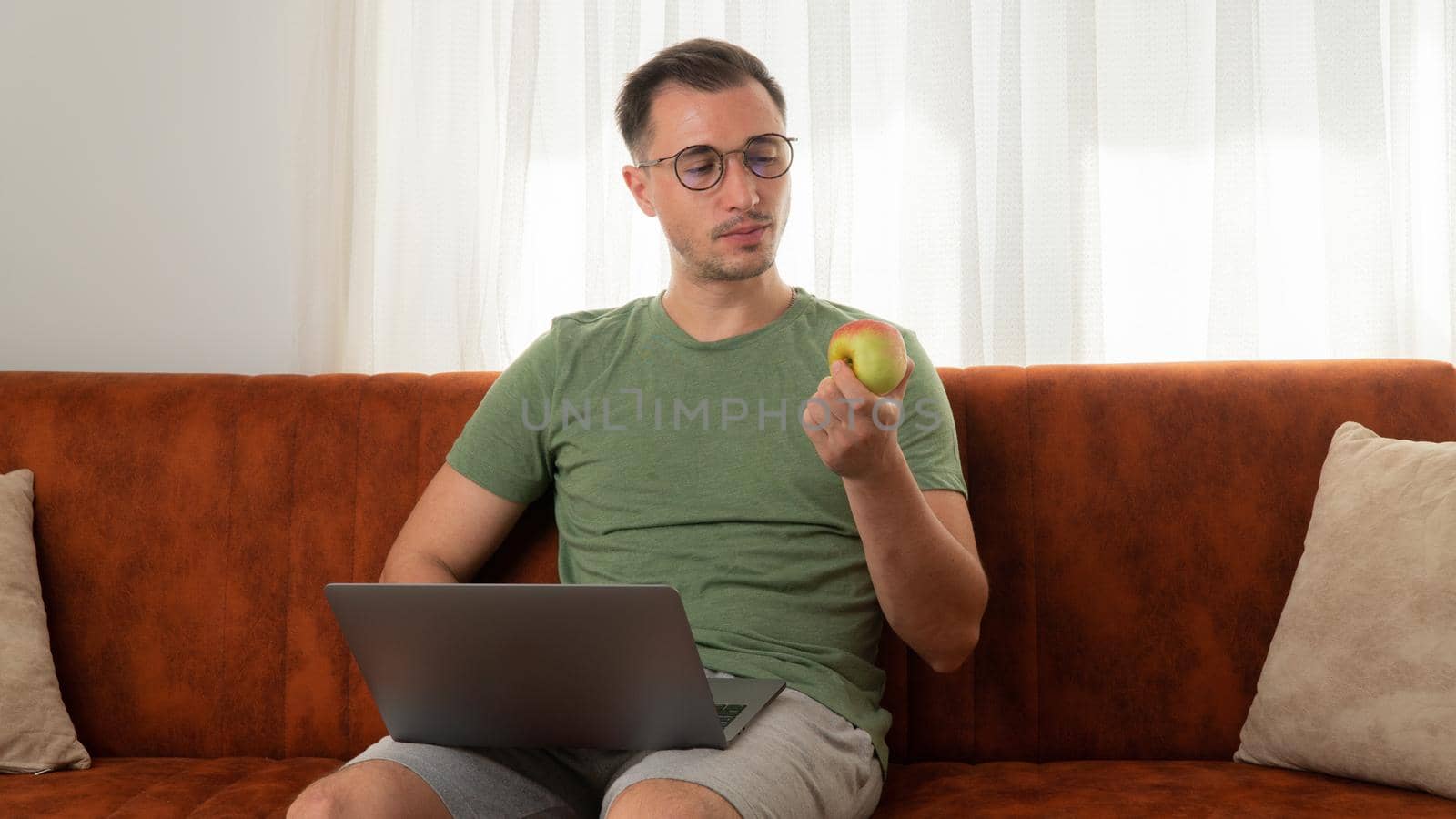 A man eats an apple on the couch with a laptop at work at home. High quality photo