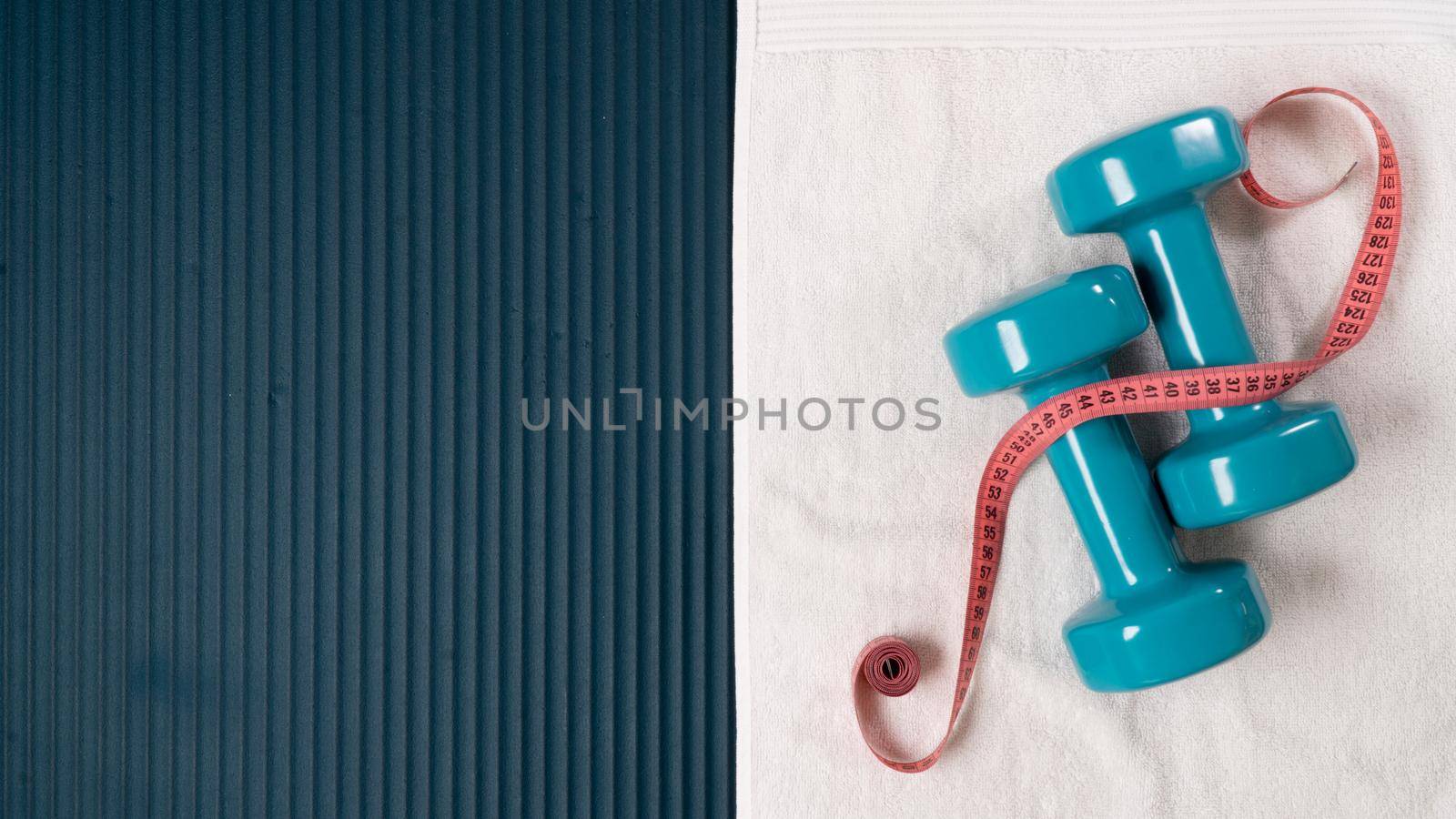Measuring tape centimeter with dumbbells and towel on the mat for training - sports background with space for text by voktybre