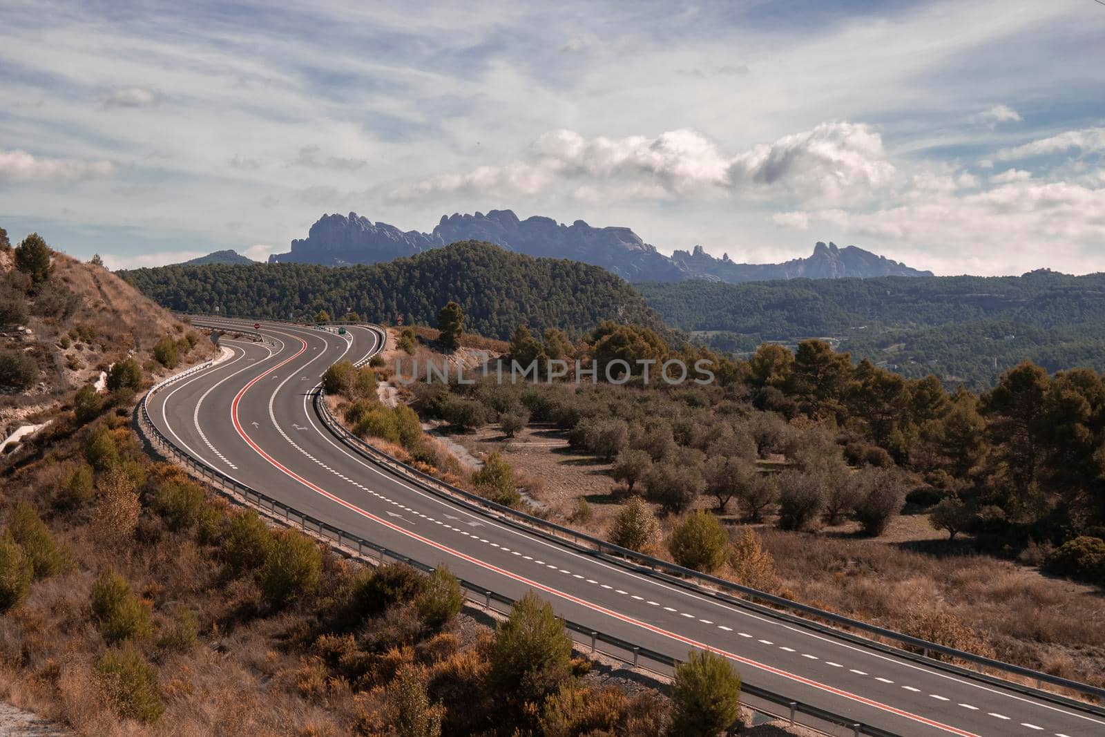 Curved road and Montserrat mountain in the background in a landscape under a cloudy sky in Catalonia
