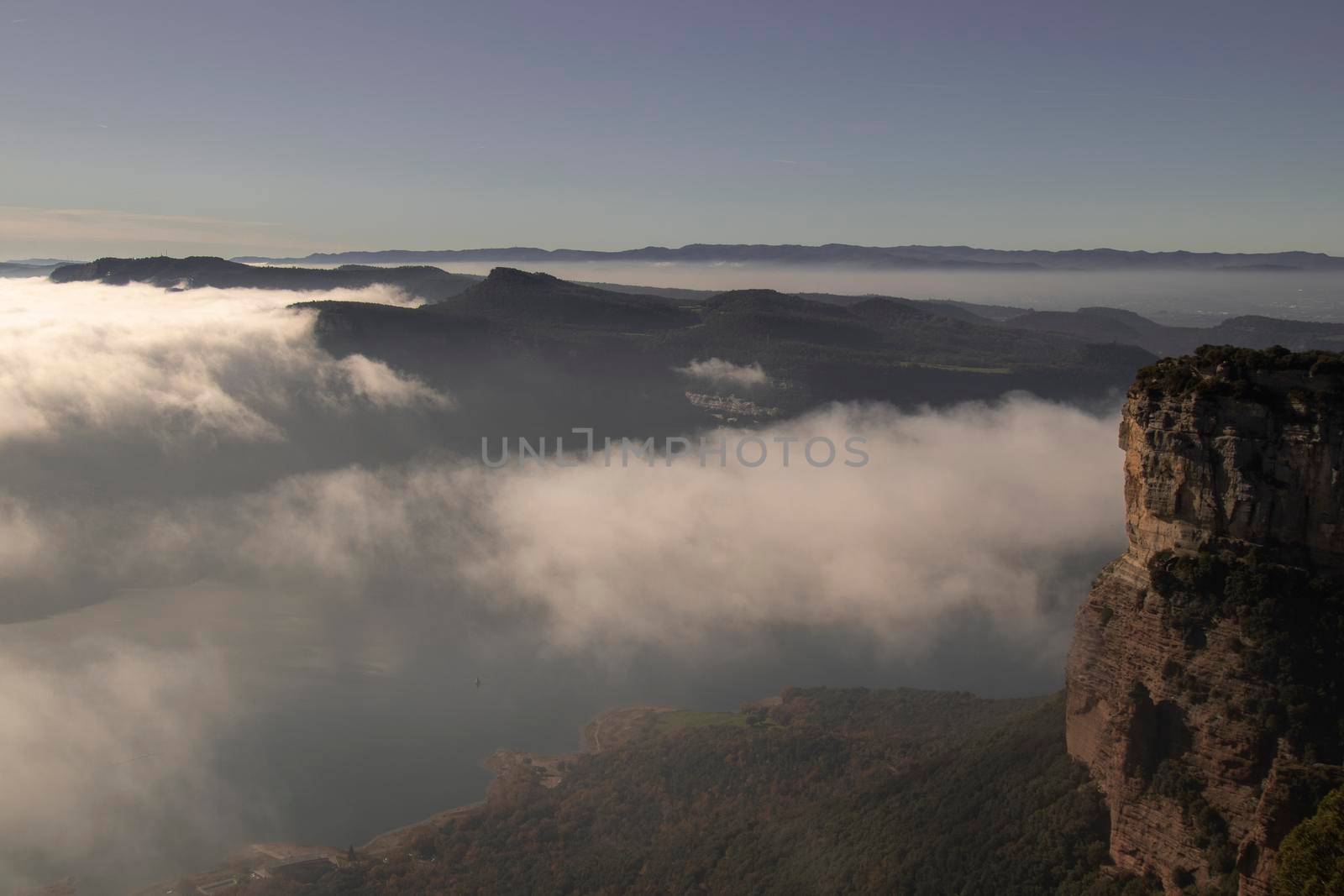 Landscape showing a cliff partially covered by a layer of fog under a blue sky in Tavertet town in Catalonia