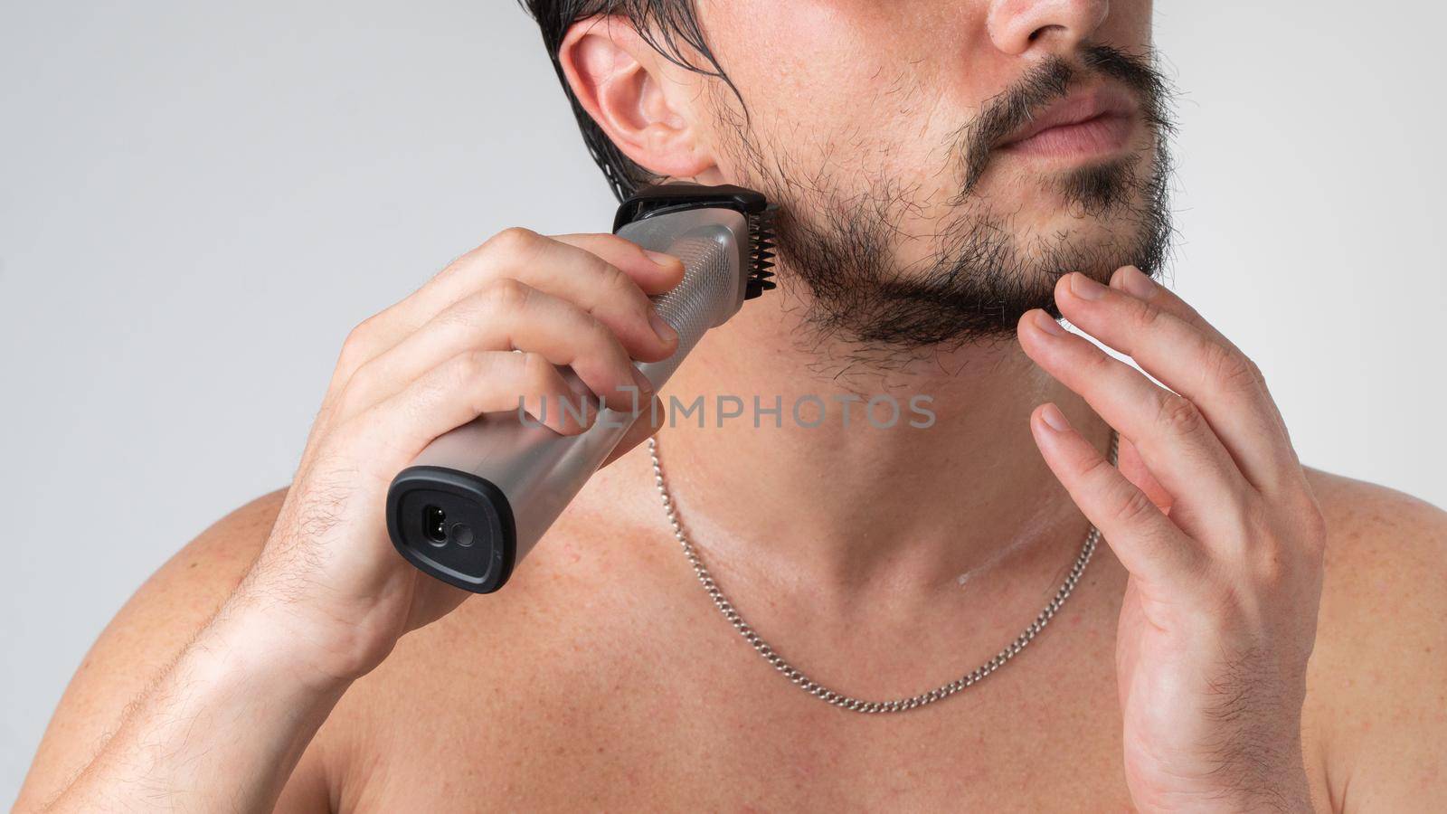 A man with an electric razor in his hands shaves his beard, close-up. High quality photo