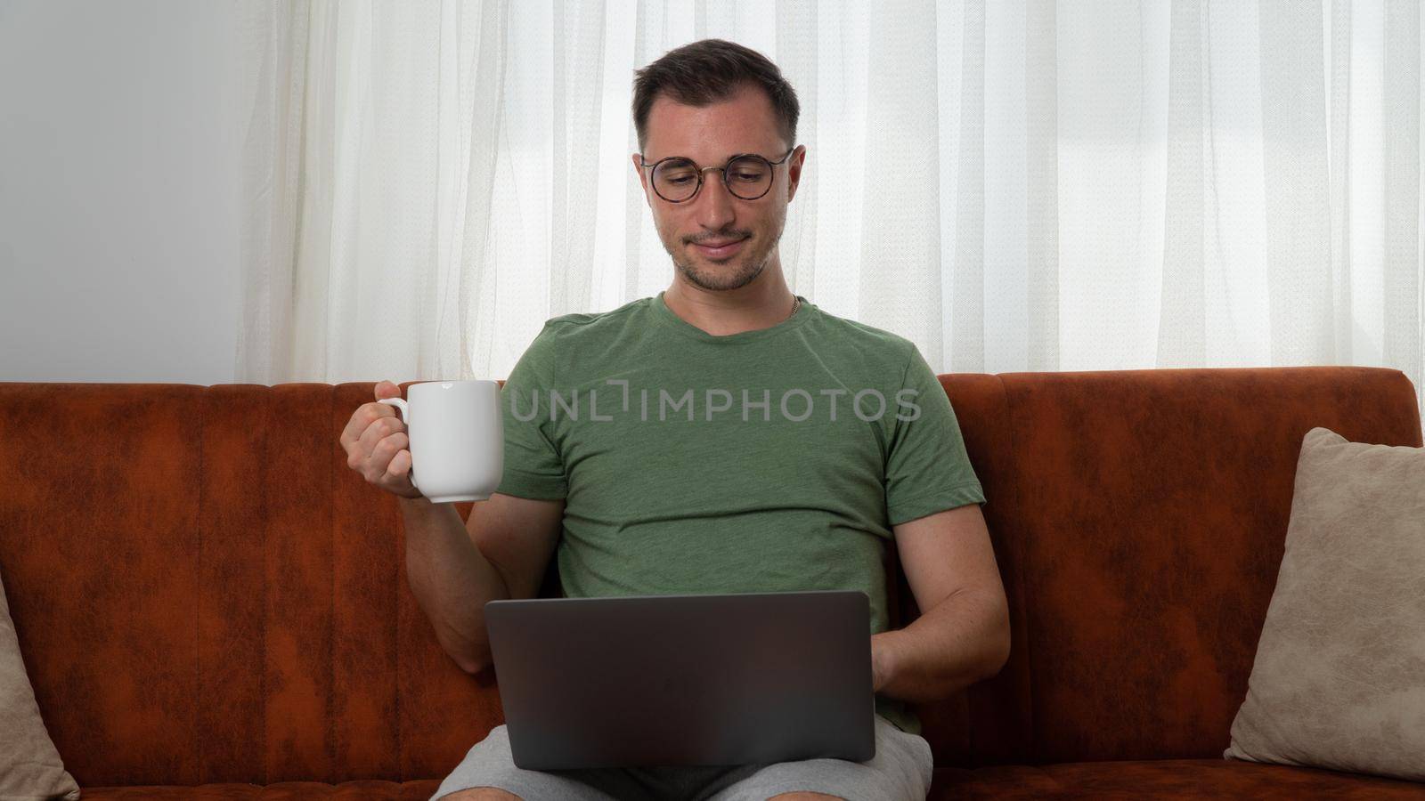 A man communicates on a laptop and drinks coffee at home, online communication. High quality photo