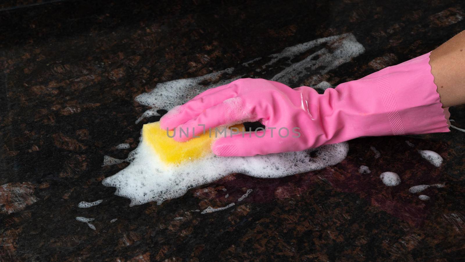 A pink rubber glove with a sponge and detergent foam washes the dirty surface. High quality photo