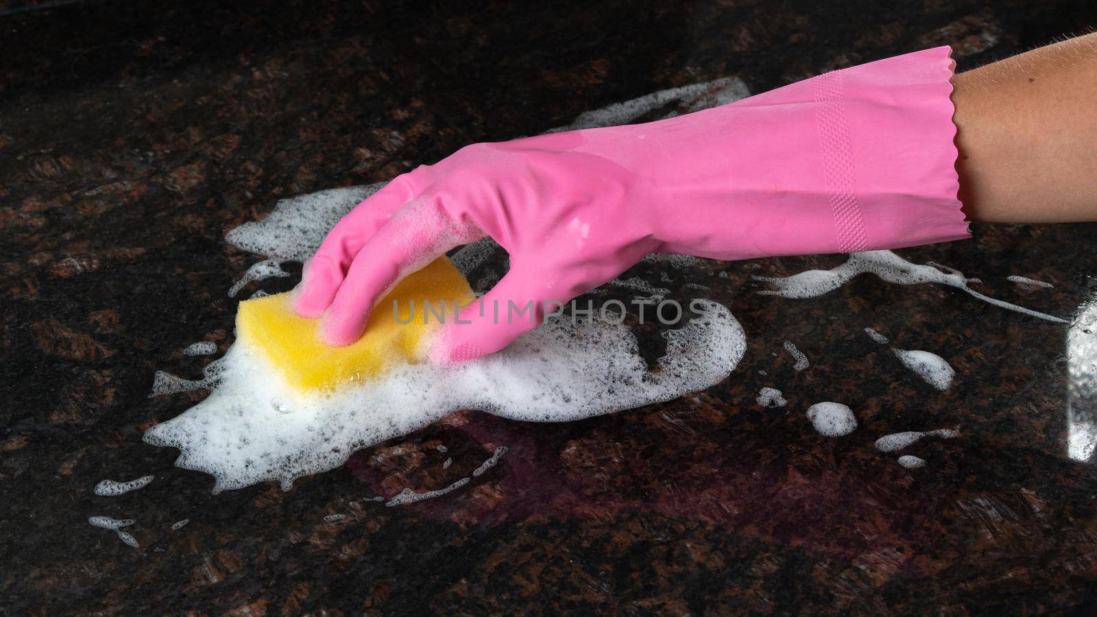 A woman's hand in a rubber glove with a sponge and foam cleans the dirty surface of the tile. High quality photo