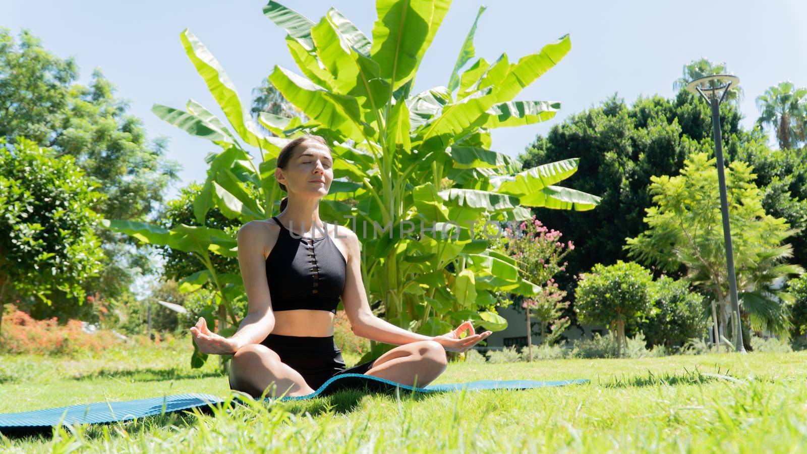 A woman sits in the lotus position and meditates in the park against the background of palm trees, yoga by voktybre