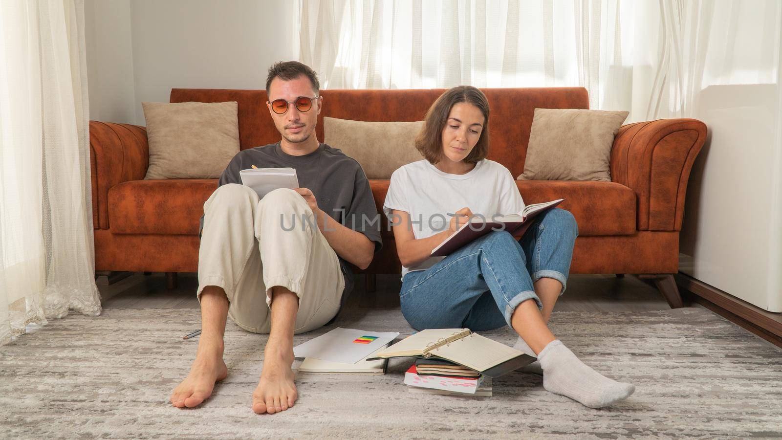 A pair of male and female students do homework while sitting on the floor. High quality photo