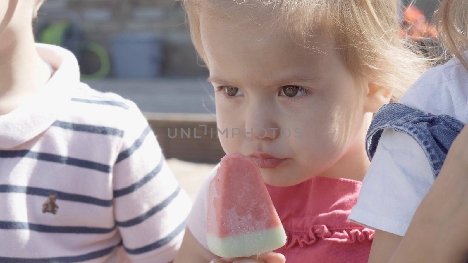 Close up portrait Girl enjoys delicious ice cream cone. Child eating watermelon popsicle. Kids Siblings snack sweets in Home Garden. Summer holiday Hot weather Sunny Day. Childhood, Food Candy Friends. by mytrykau