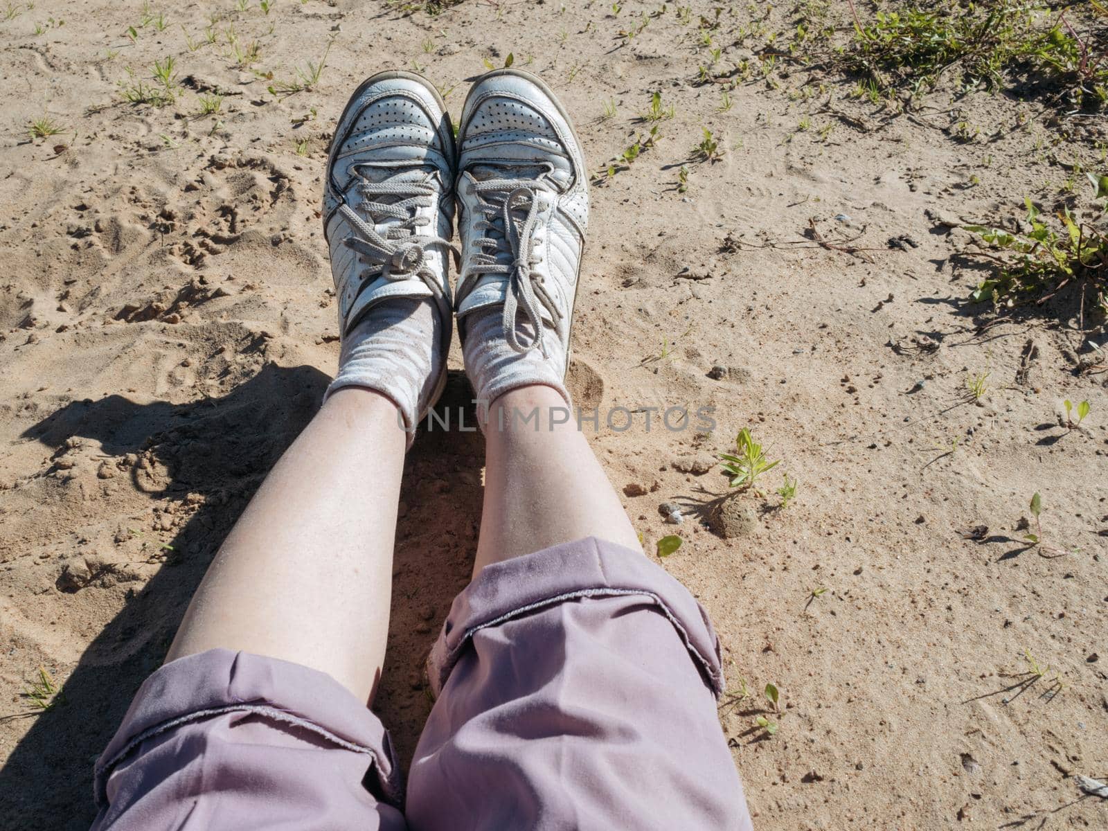 Woman's legs wearing pink pants and white sneakers laying at the beach. Sunny day. Copy space