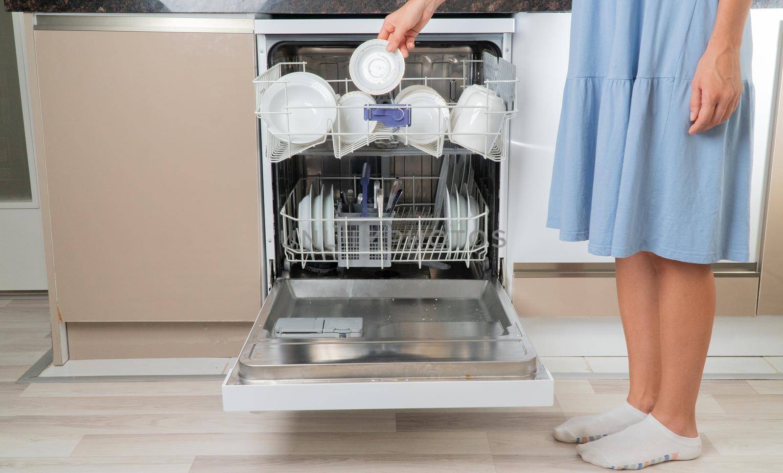 Housewife removes clean dishes from dishwasher front view