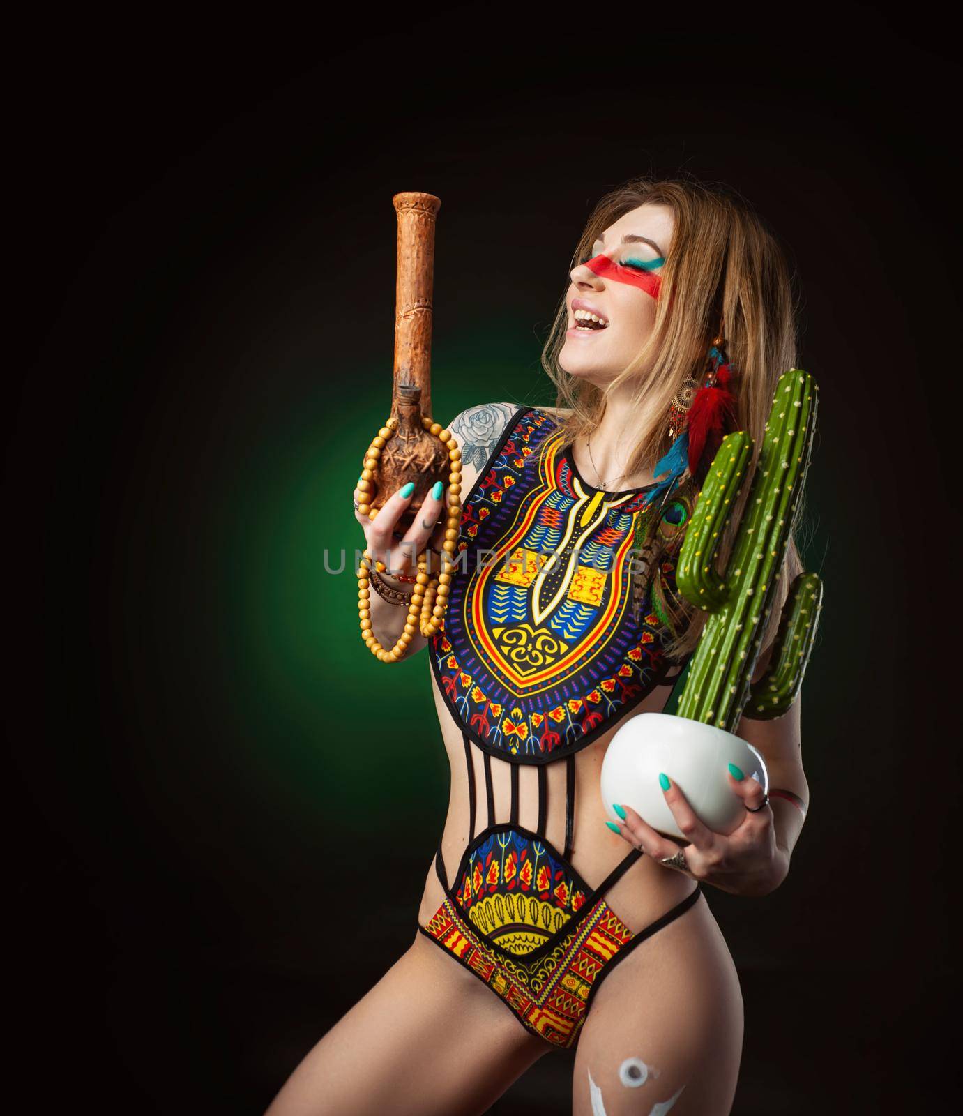 the sexy hippie girl posing with bong for smoking marijuana in a bright swimsuit on a dark background