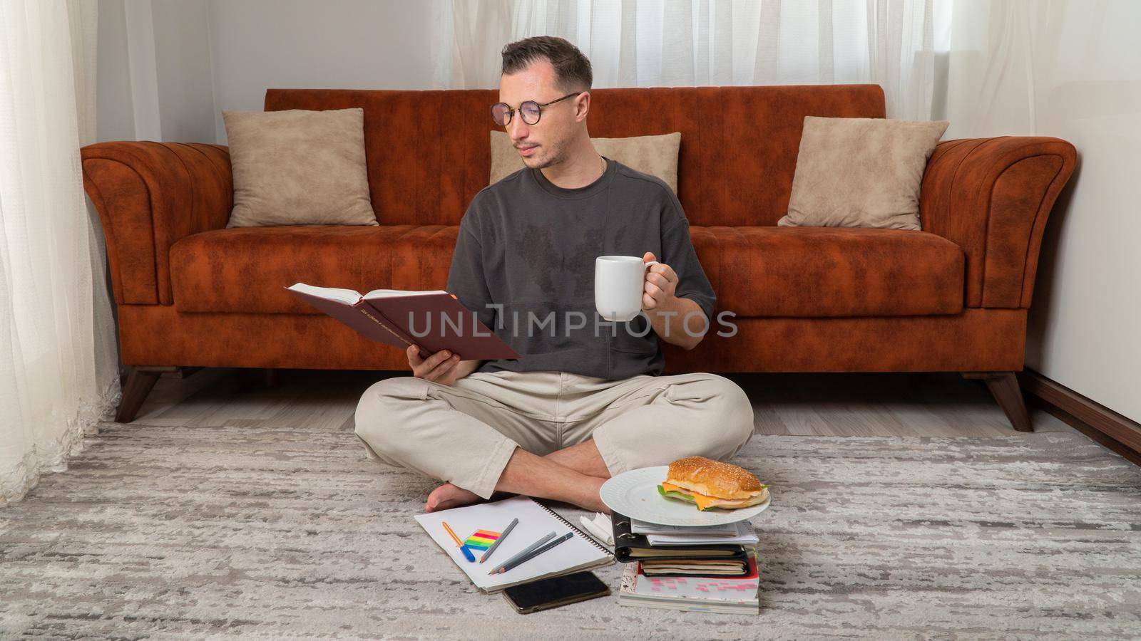 Male student drinks coffee and reads a book, studies at home, snacks. High quality photo