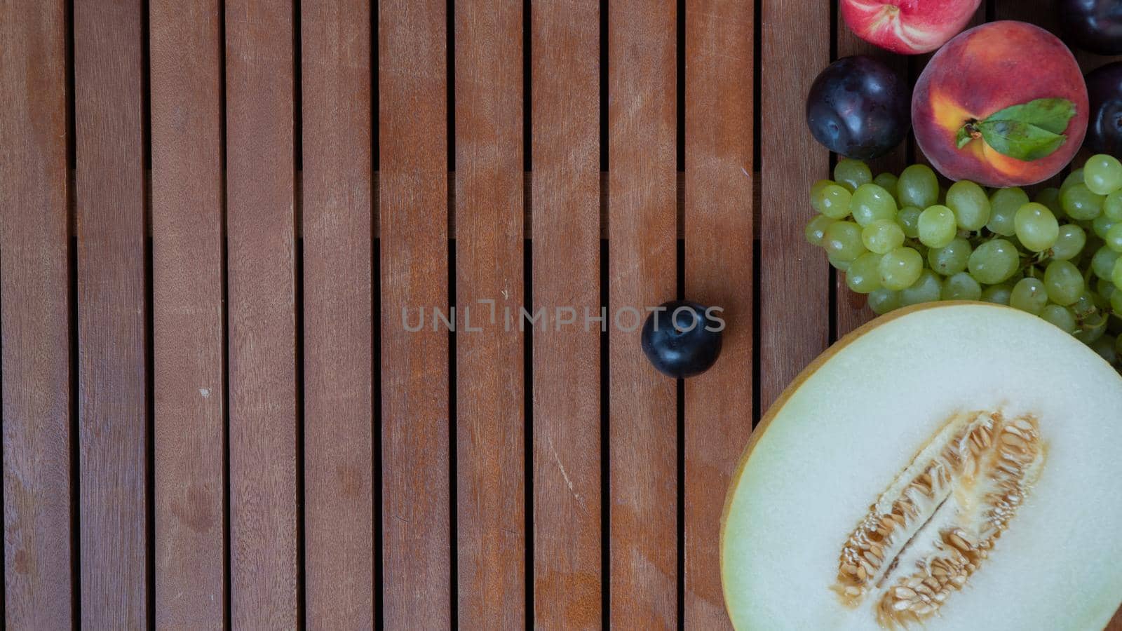 Melon, plum, grape and peach on a wooden background with space for text by voktybre