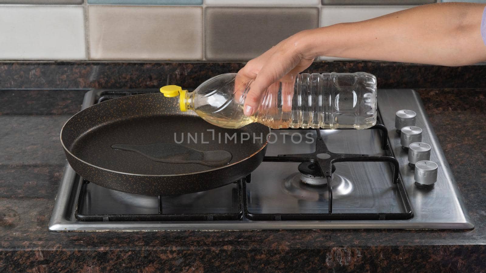 A woman pours sunflower oil into a frying pan on a gas stove close-up