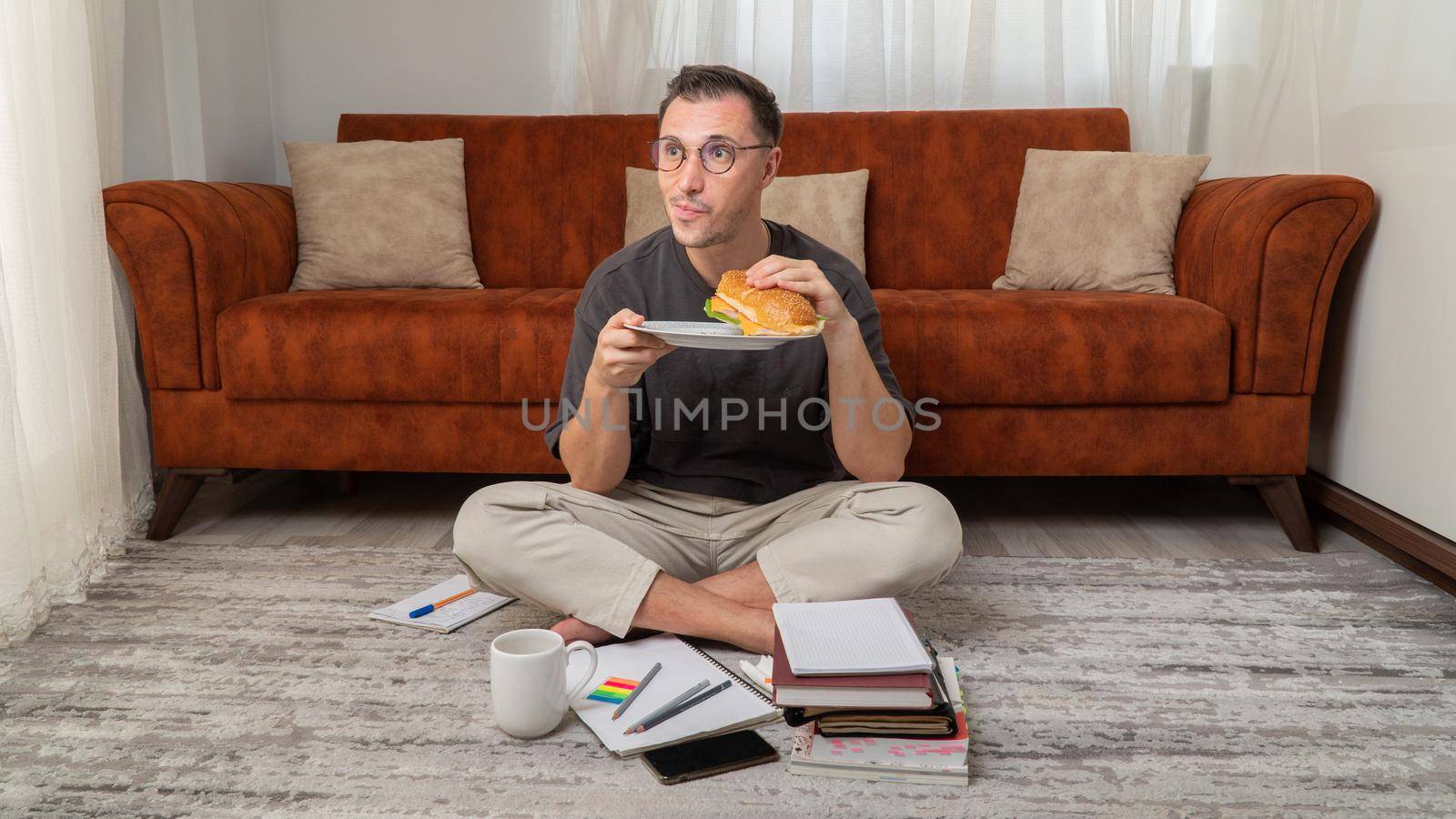 Student eats a large sandwich while studying at home. High quality photo