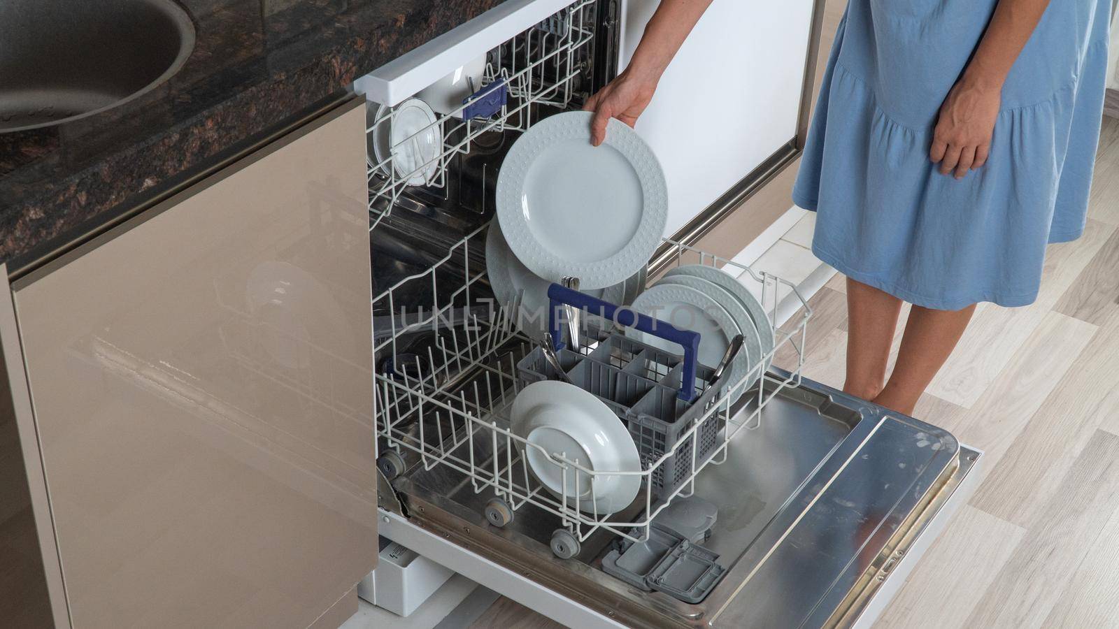 Housewife pulls clean plates out of dishwasher close-up