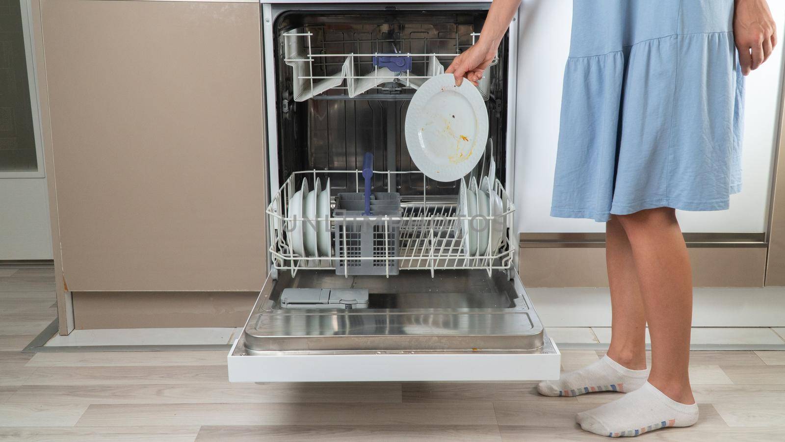A housewife puts loading dirty dishes into the dishwasher front view
