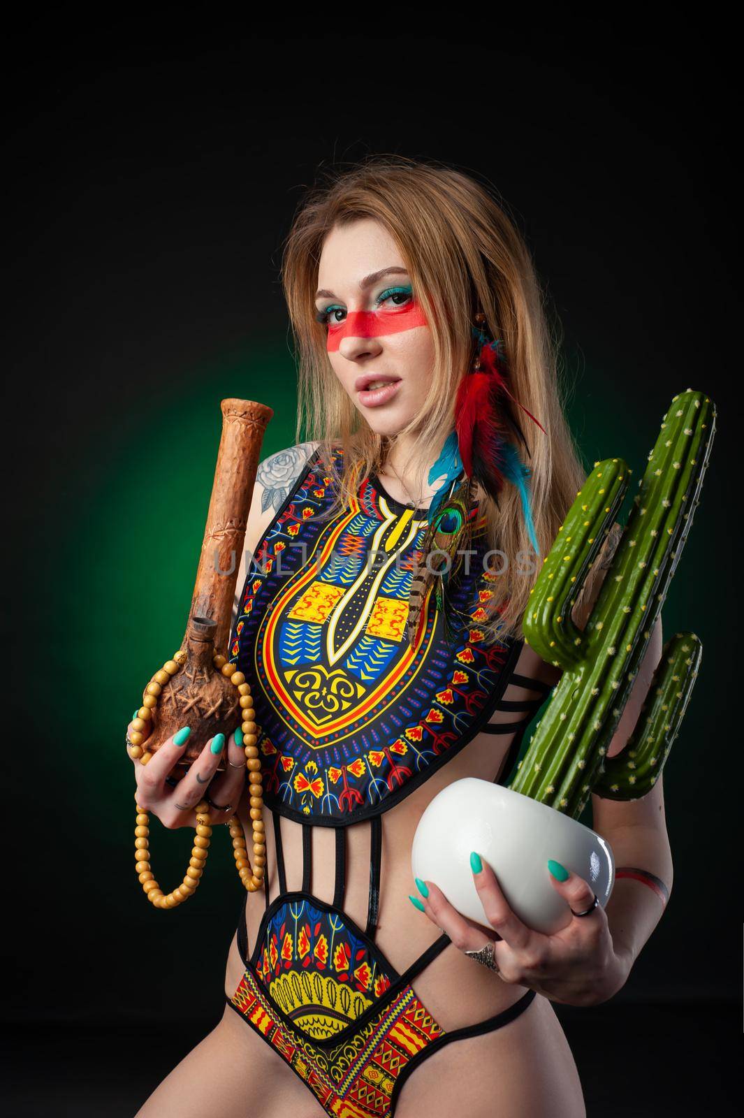 the sexy hippie girl posing with bong for smoking marijuana in a bright swimsuit on a dark background