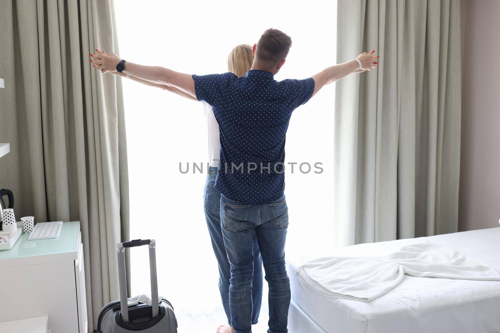 Married couple hugging and holding hands at window of hotel room in bedroom by kuprevich