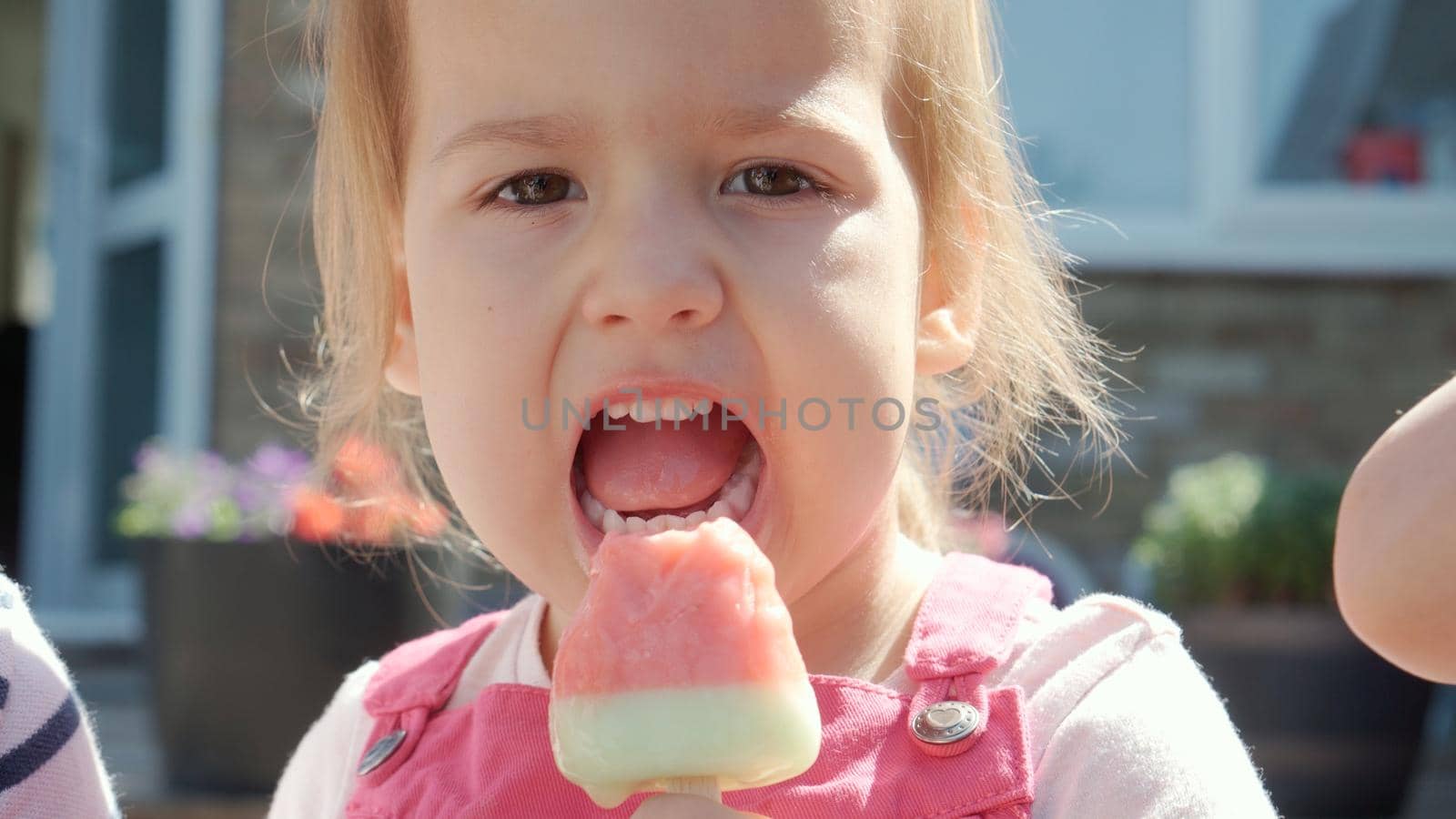 Close up portrait Girl enjoys delicious ice cream cone. Child eating watermelon popsicle. Kids Siblings snack sweets in Home Garden. Summer holiday Hot weather Sunny Day. Childhood, Food Candy Friends