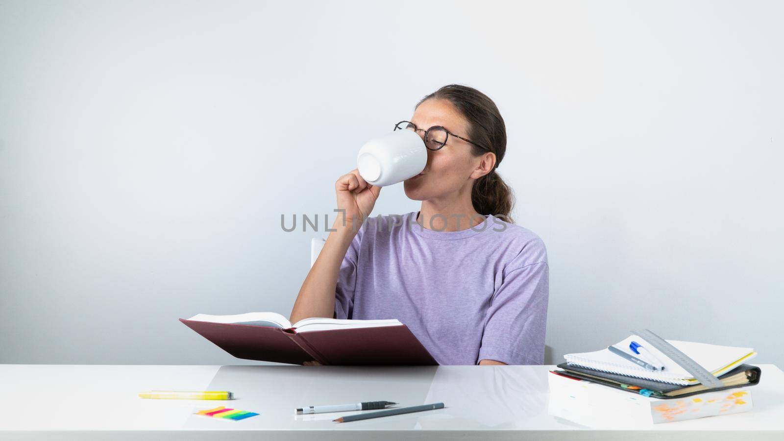 A student learns lessons and drinks tea while reading a textbook - a break for rest. High quality photo