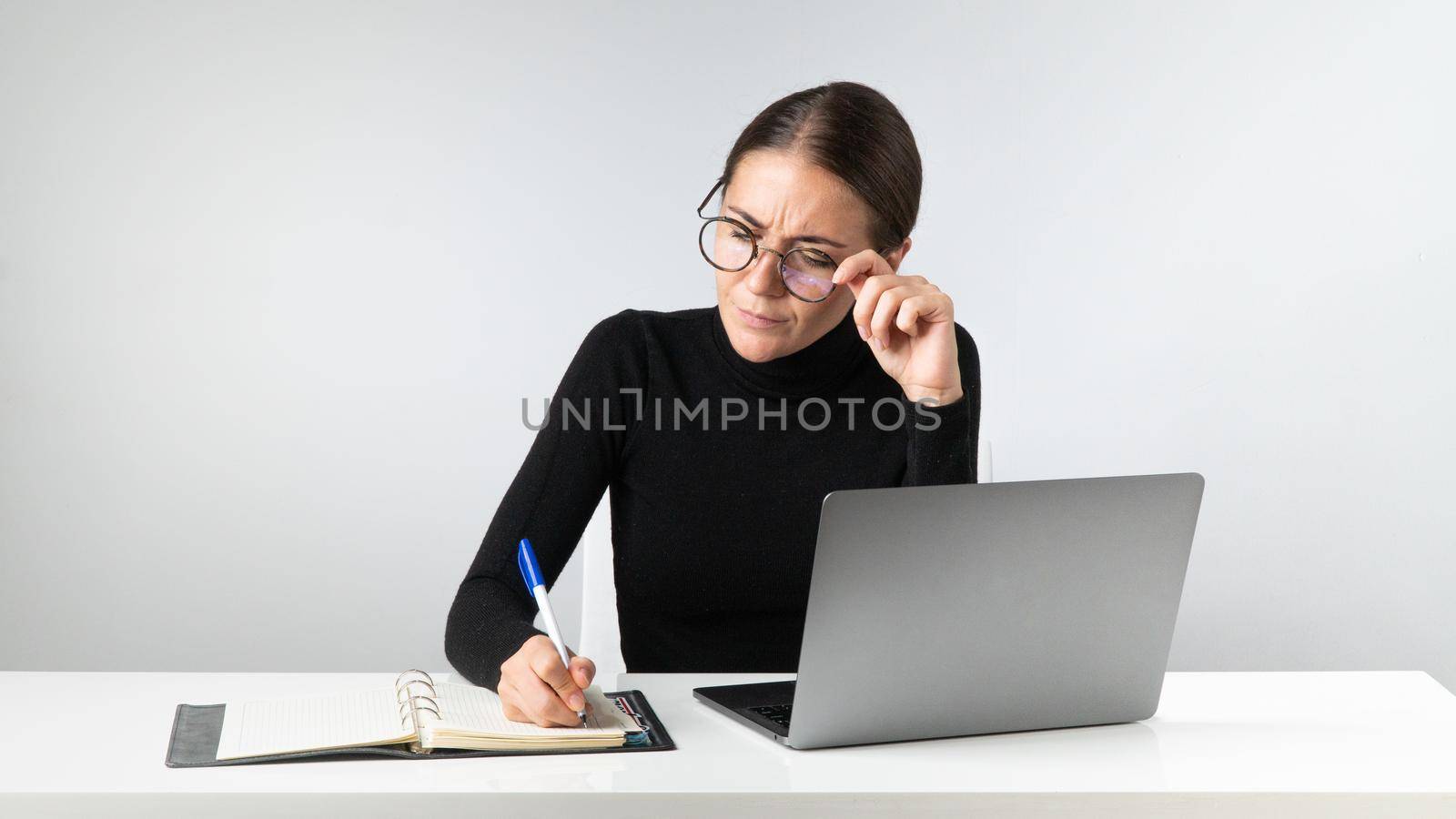 A serious businesswoman works in the office on a laptop, takes notes in a notebook by voktybre