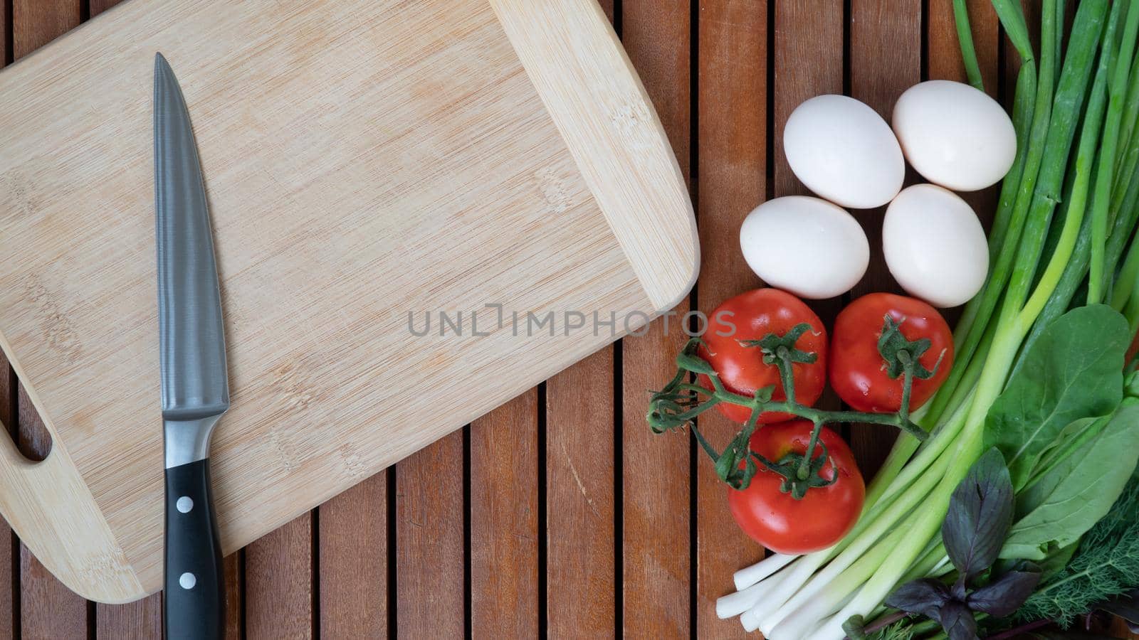 Vegetables greens, eggs on the table with a board and a knife for cooking by voktybre