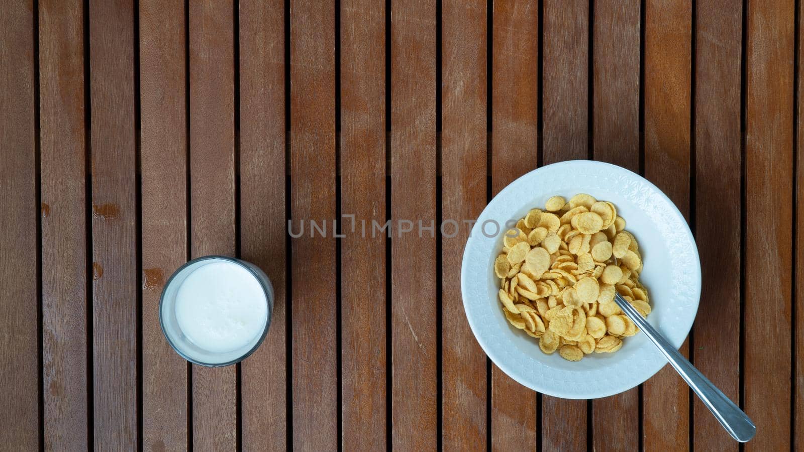 A plate of corn flakes on the right and a glass of milk on the left background. High quality photo