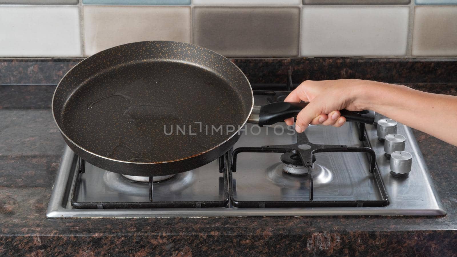 A woman's hand holds a frying pan of oil over a gas stove by voktybre