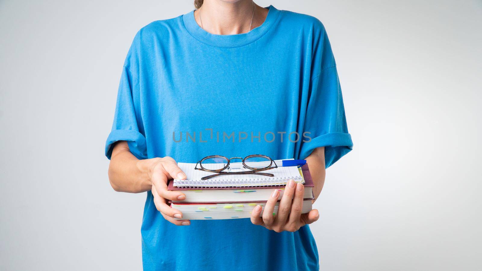 On a stack of textbooks and notebooks are glasses with transparent glasses in the hands of a student. High quality photo