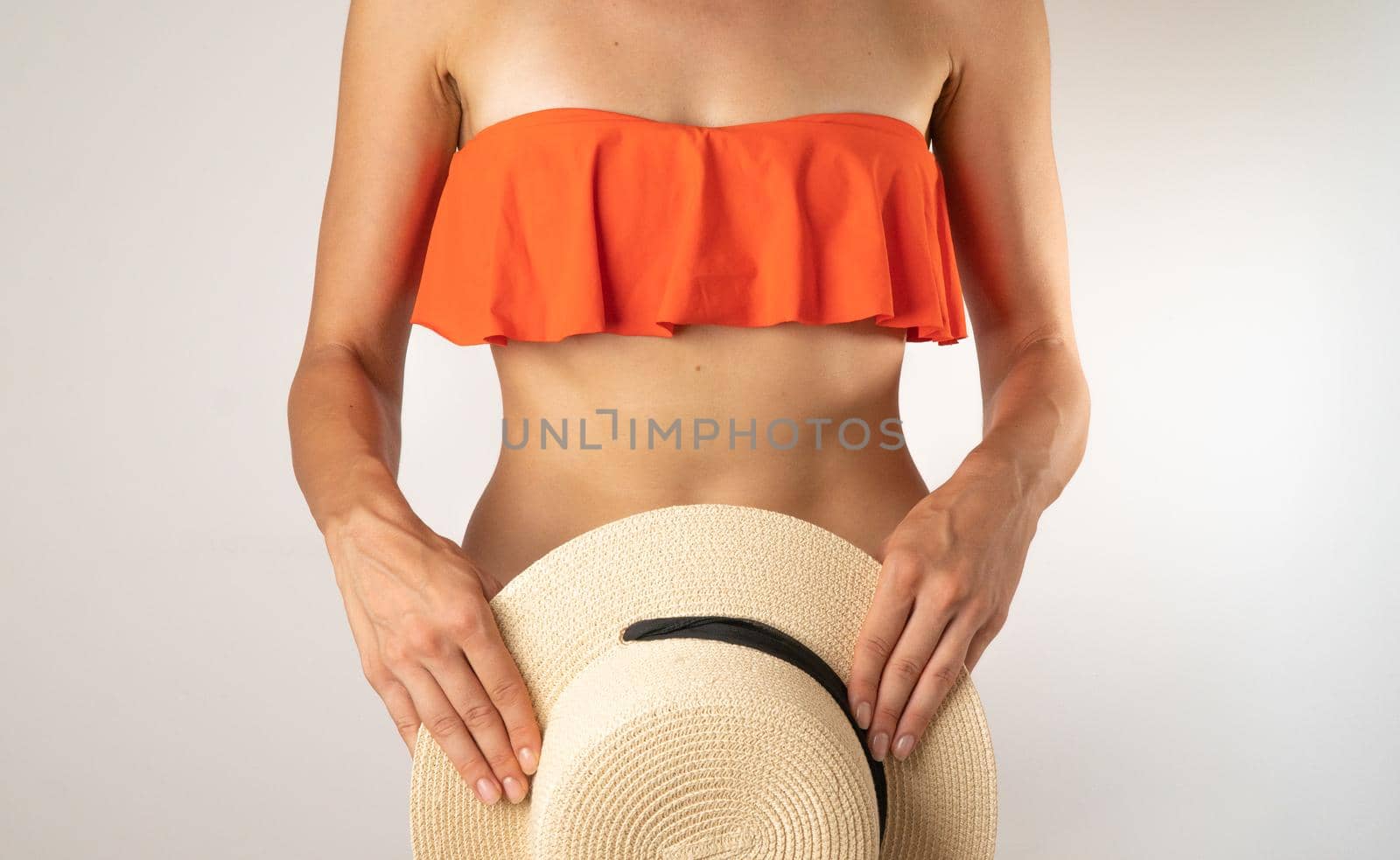 Slender female body in an orange swimsuit top, the bottom covers with a straw hat - summer. High quality photo