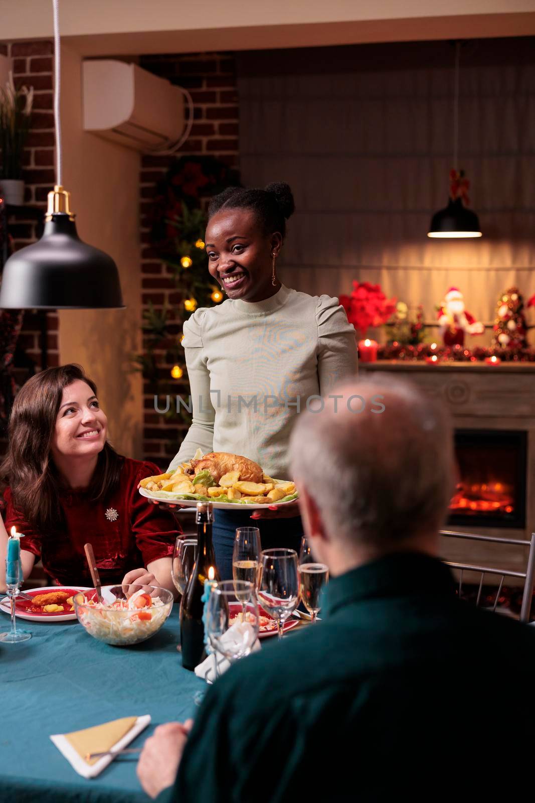 Family christmas celebration, friends gathering at festive dinner table, smiling woman holding traditional chicken. Happy diverse people eating xmas dishes, winter holiday party
