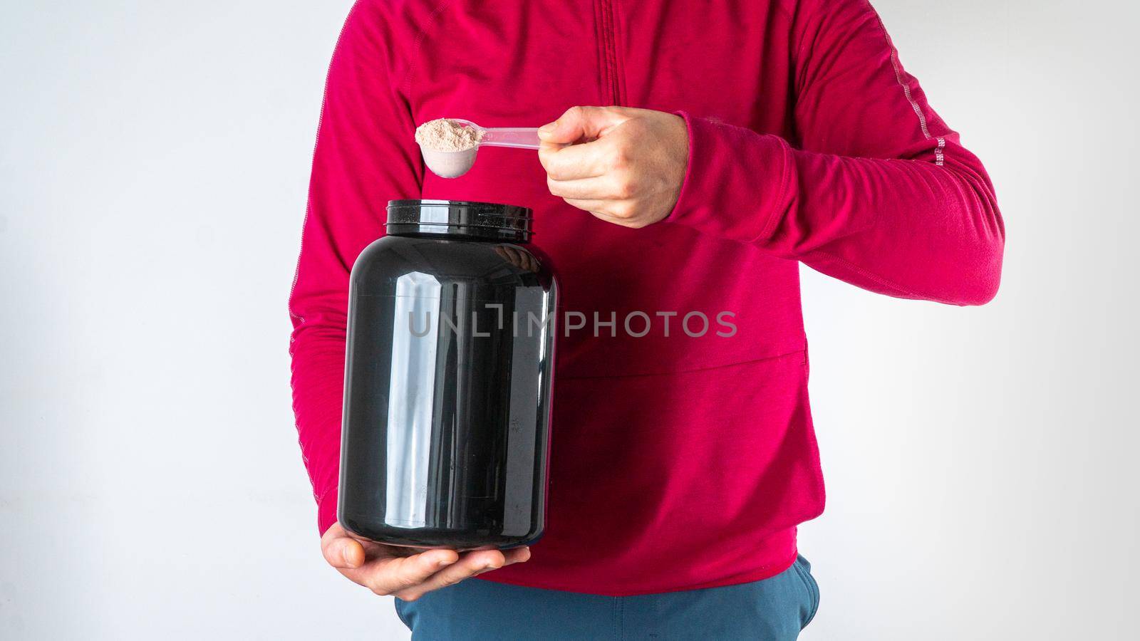 A man in a sports jacket with a can of sports nutrition puts protein into the measuring spoon. High quality photo
