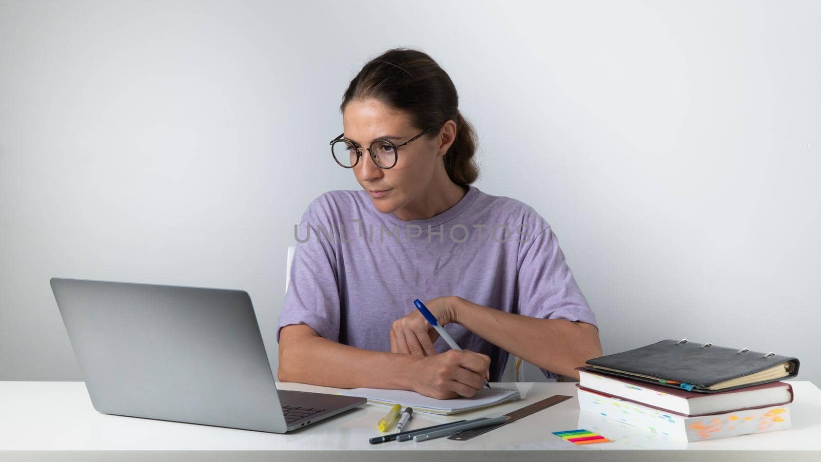 A woman with a laptop, books, notebooks, notebooks at the table makes notes - online learning, remote work by voktybre
