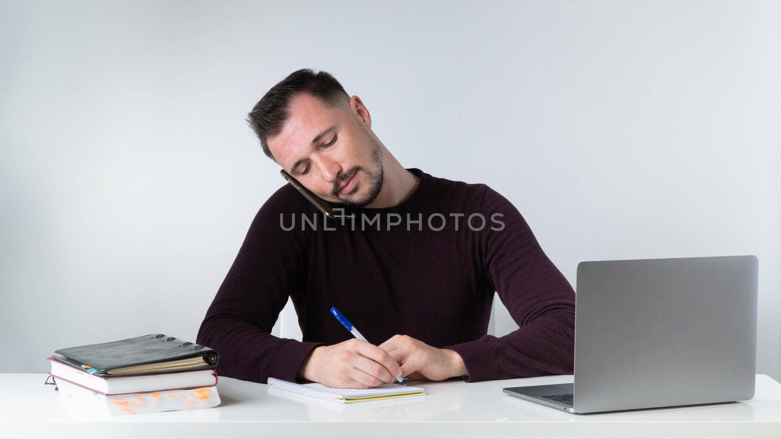 A man talks on the phone and records information in the office at his desk. by voktybre