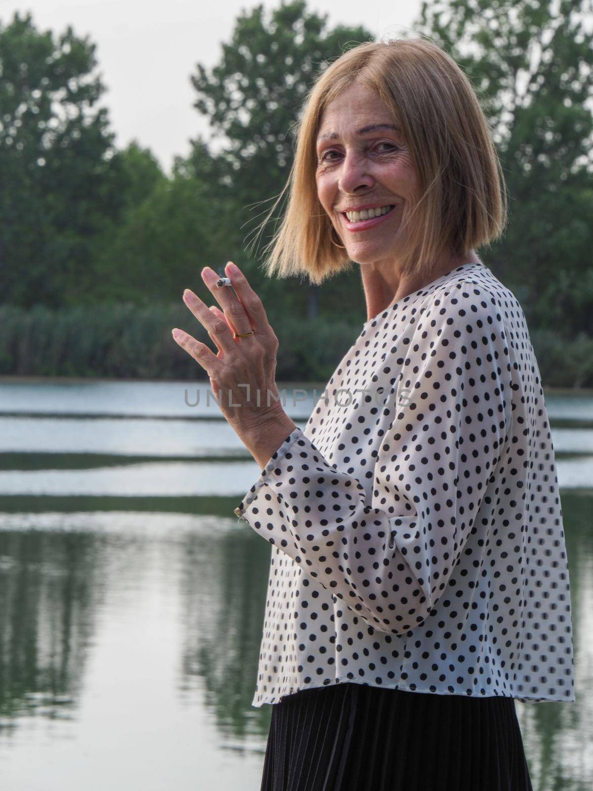 female pensioner having fun and smoking a cigarette in a park - aging free and wellness concept