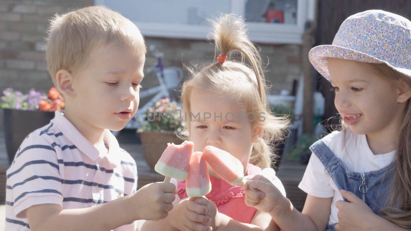Three cute little Children enjoys delicious ice cream cone. Child eating watermelon popsicle. Kids Siblings snack sweets in Home Garden. Summer holiday Hot weather Sunny Day. Childhood, Food Candy by mytrykau
