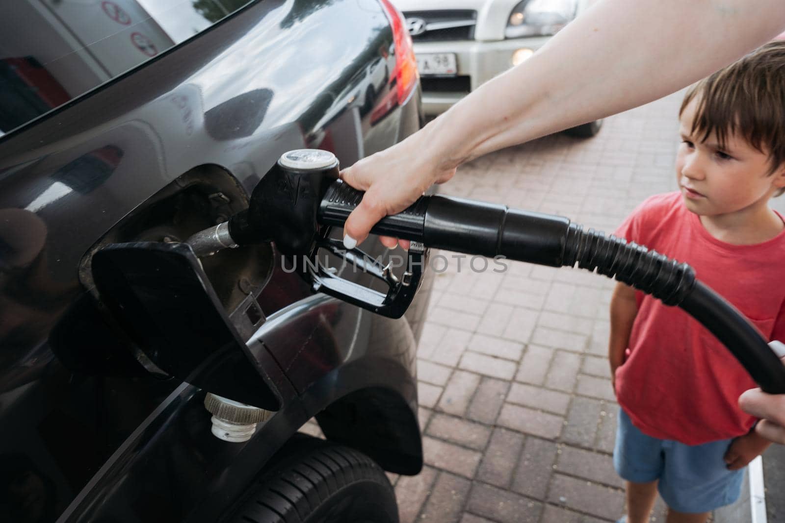 Closeup of a Fueling a car at the gas station. Small boy is standing. next to the car and looking