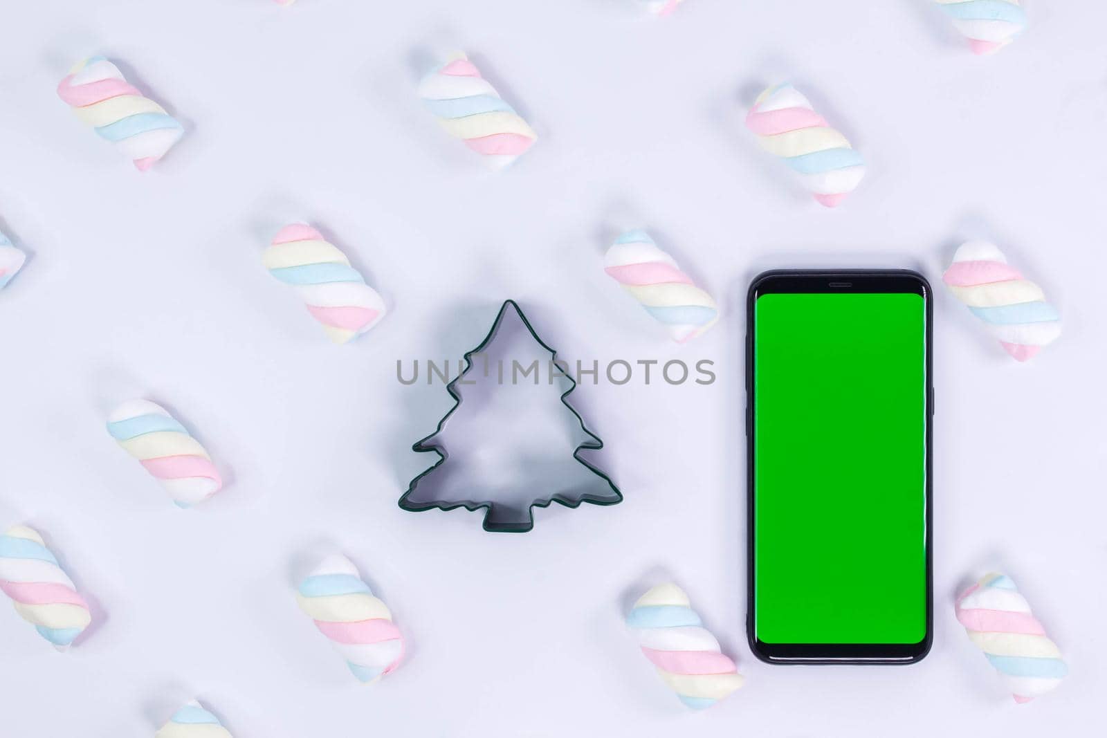 Smartphone with a vertical green screen on white. Christmas tree cooky cutter. White background with twisted marshmallow pattern. Chroma key smartphone technology. Phone mockup