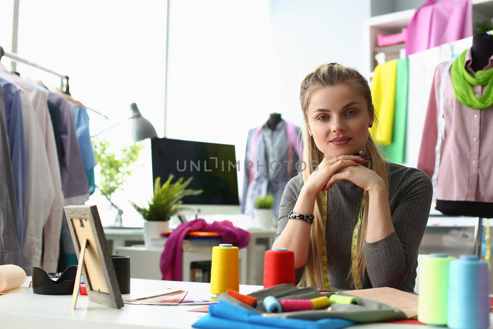 Portrait of smiling young dressmaker or tailor sewing fabric creates new clothes in own workshop. Happy designer or seamstress in fashion atelier