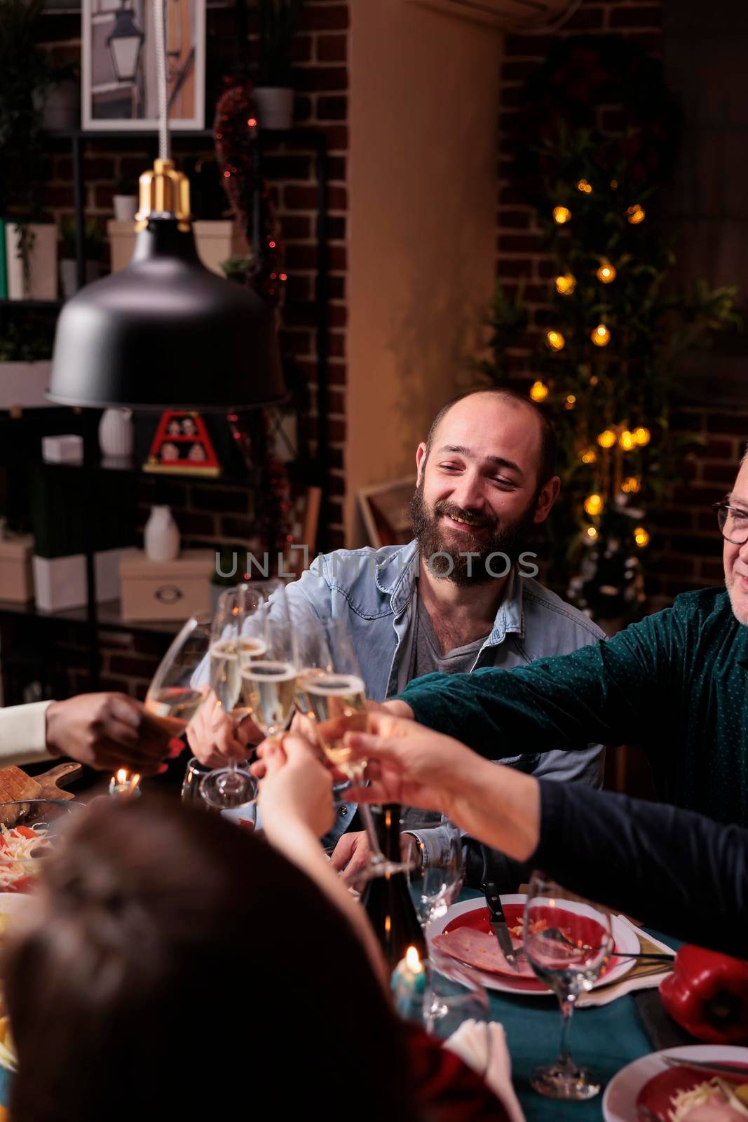 People clinking glasses with sparkling wine, proposing christmas toast at festive dinner. Winter holiday celebration with parents, family gathering together, drinking at new year party