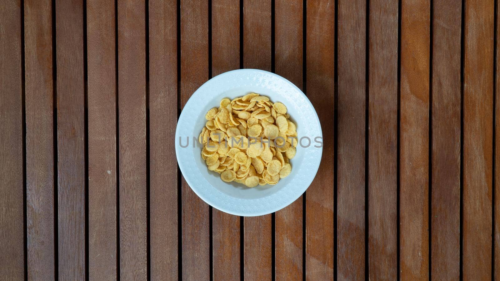 Corn flakes in a white plate in the middle on a wooden background for breakfast by voktybre