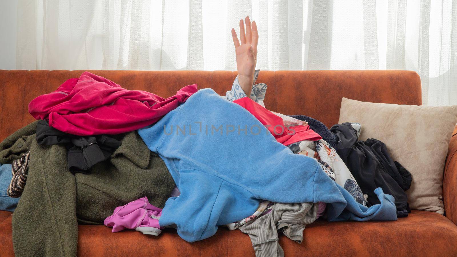 Dependence on things, conscious consumption of clothes, shopaholic, hand reaching out of a pile of clothes. High quality photo