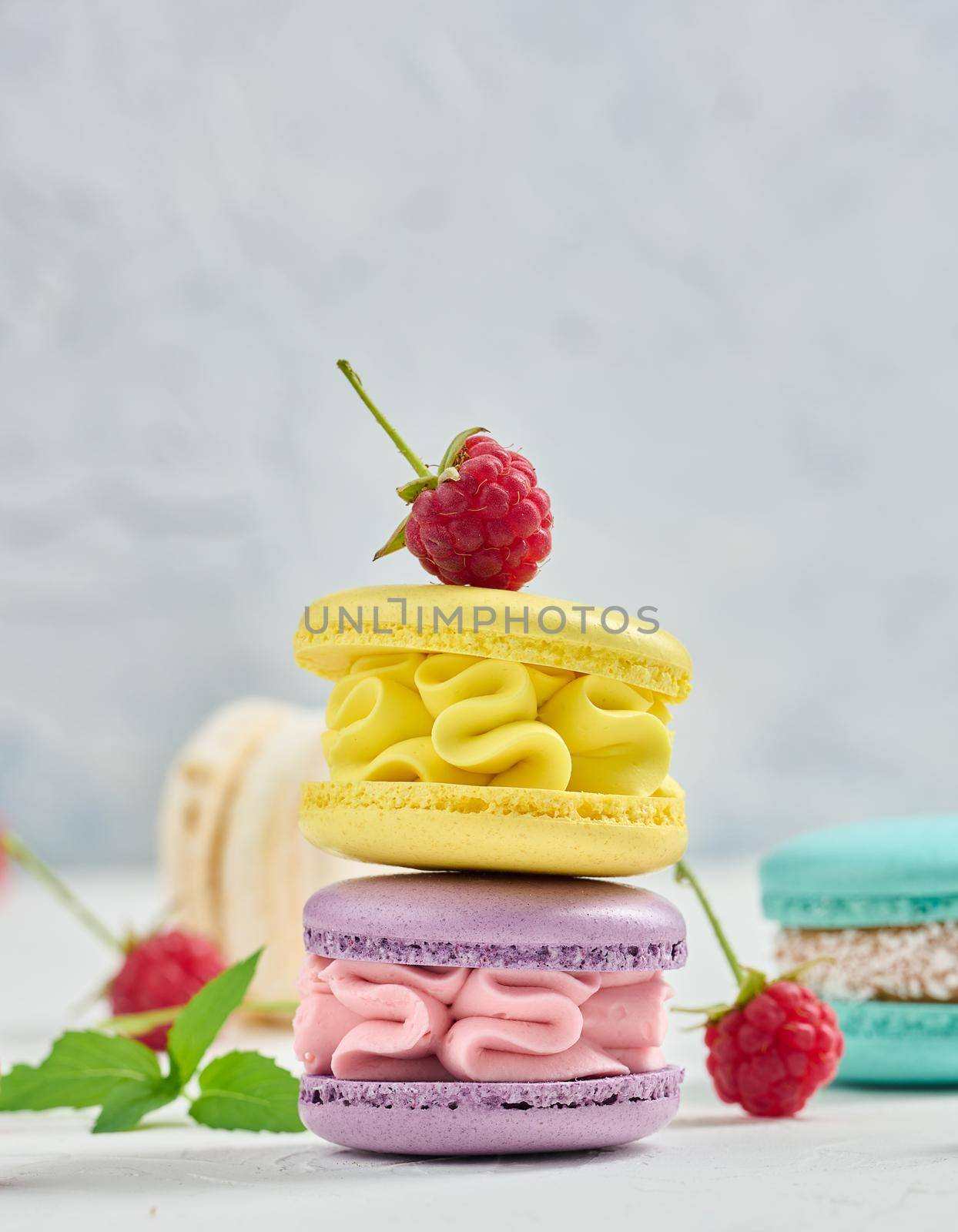 A stack of multicolored macaroons and red raspberries on a white background. by ndanko