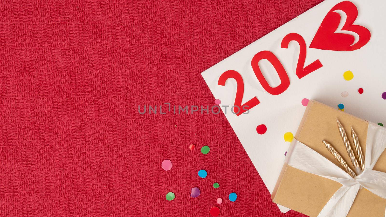 the number 2023 next to the gift box on a red background with confetti, new year. High quality photo