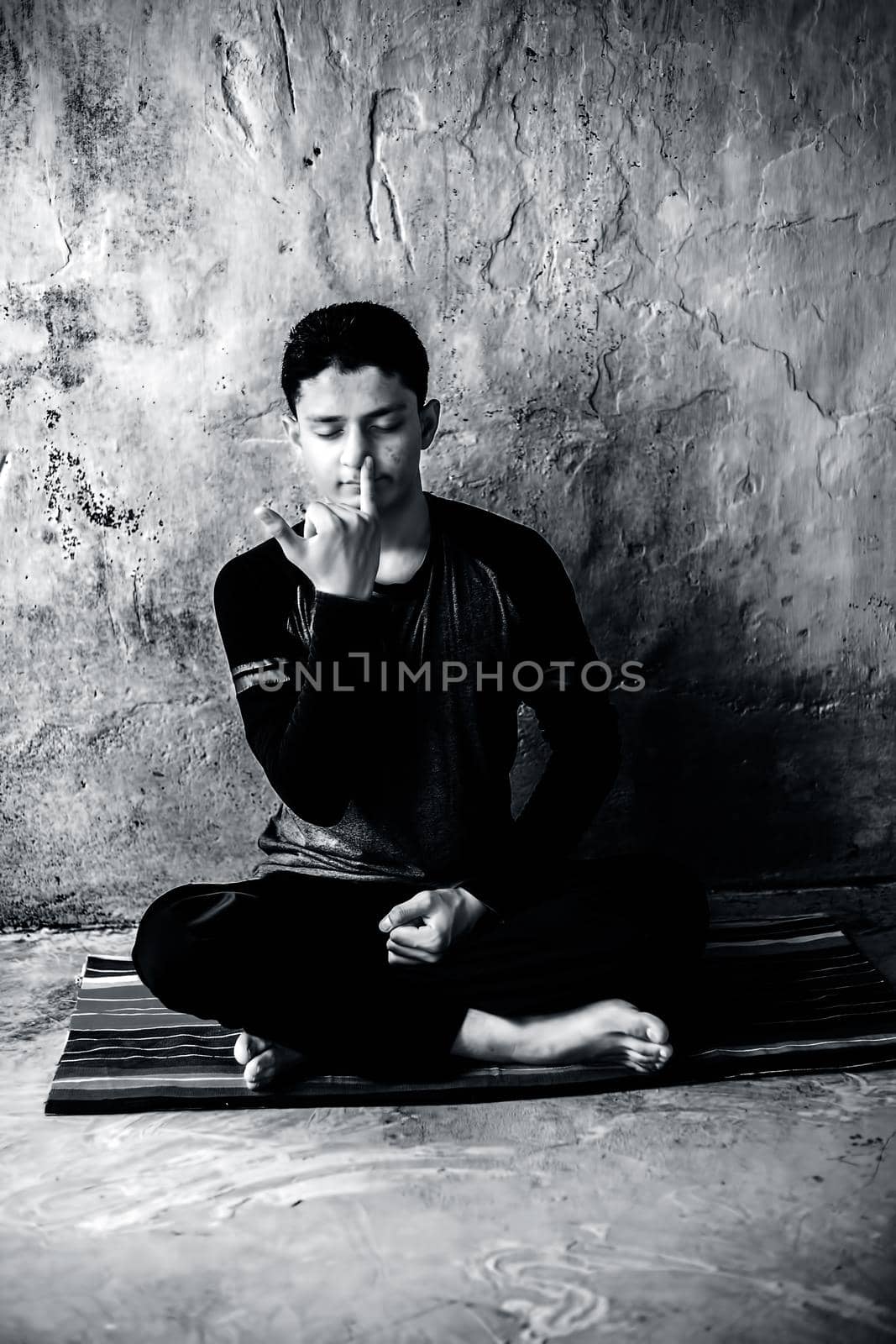 Portrait shot of the young man doing pranayama or pranayam or breath control yoga on a colorful mat with wearing black attire.