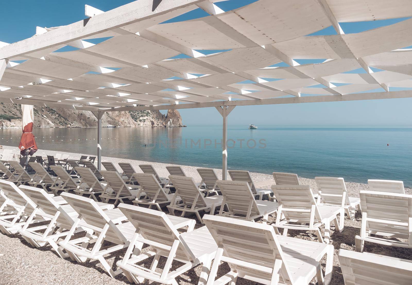 Empty sun loungers under a canopy on the beach. The beach area is empty. No people. White plastic sunbeds under the sun shade. The holiday season ends. Holiday season begins. Waiting for tourists