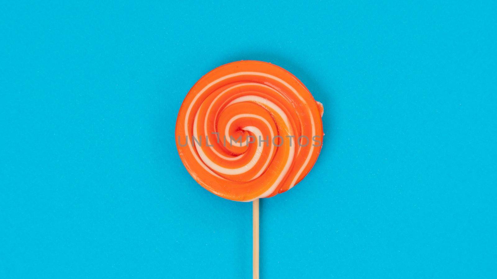 Round orange lollipop on a stick on a blue background - juicy sweet background by voktybre