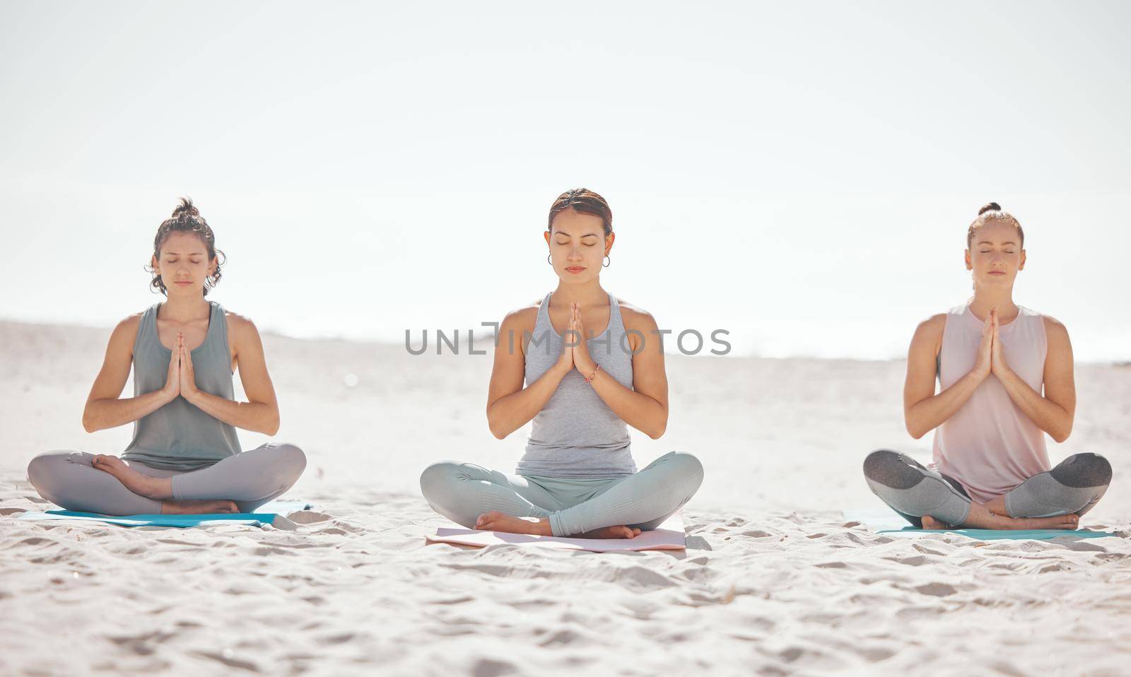 Beach meditation, women or zen friends in mental health wellness exercise, pilates training or mind reiki energy yoga. Relax, namaste prayer hands or people in peace breathing support workout on sand.
