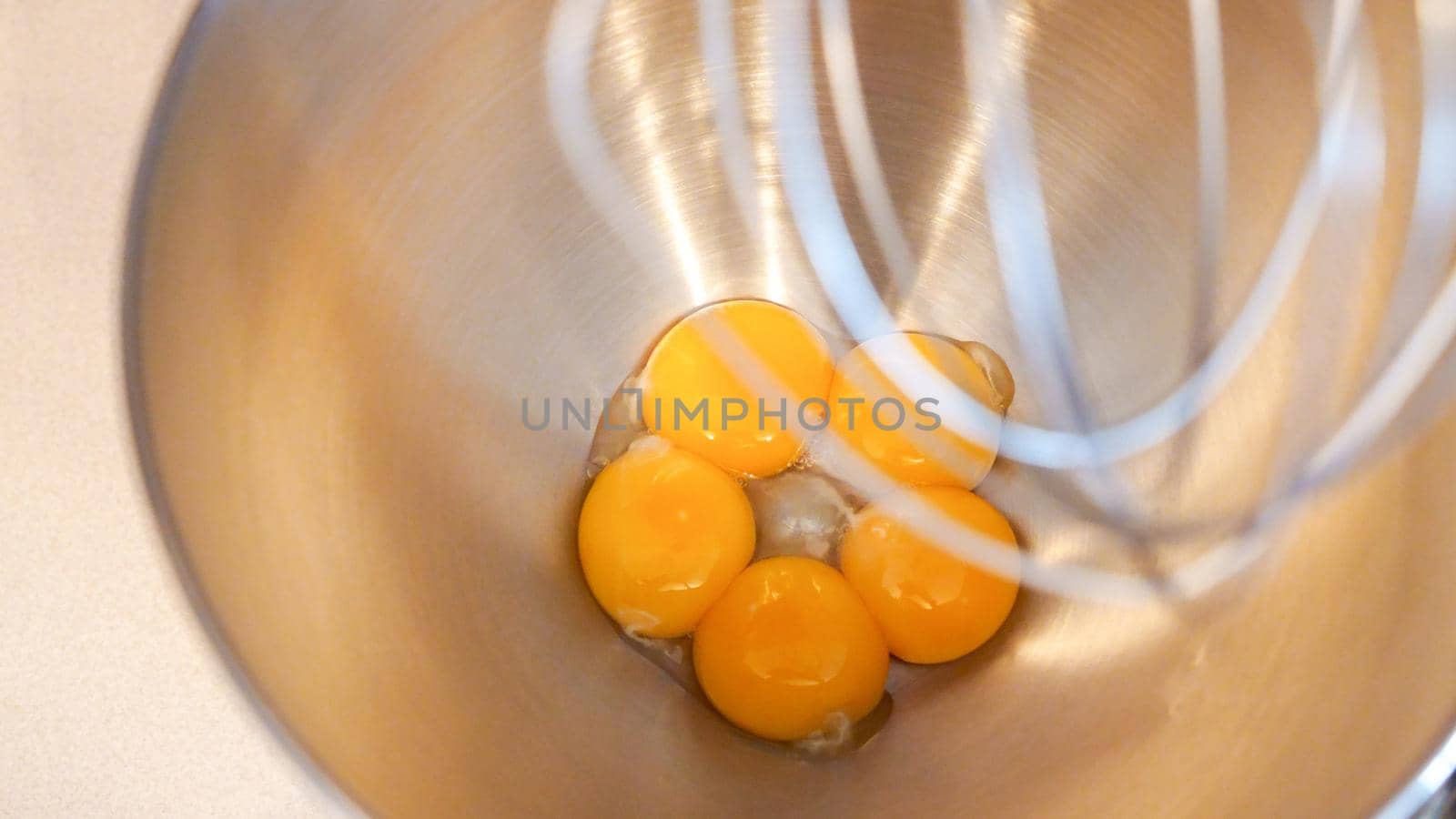 Raw eggs in a metal bowl of standing mixer. Preparing egg yolk with sugar in kitchen mixer. by JuliaDorian