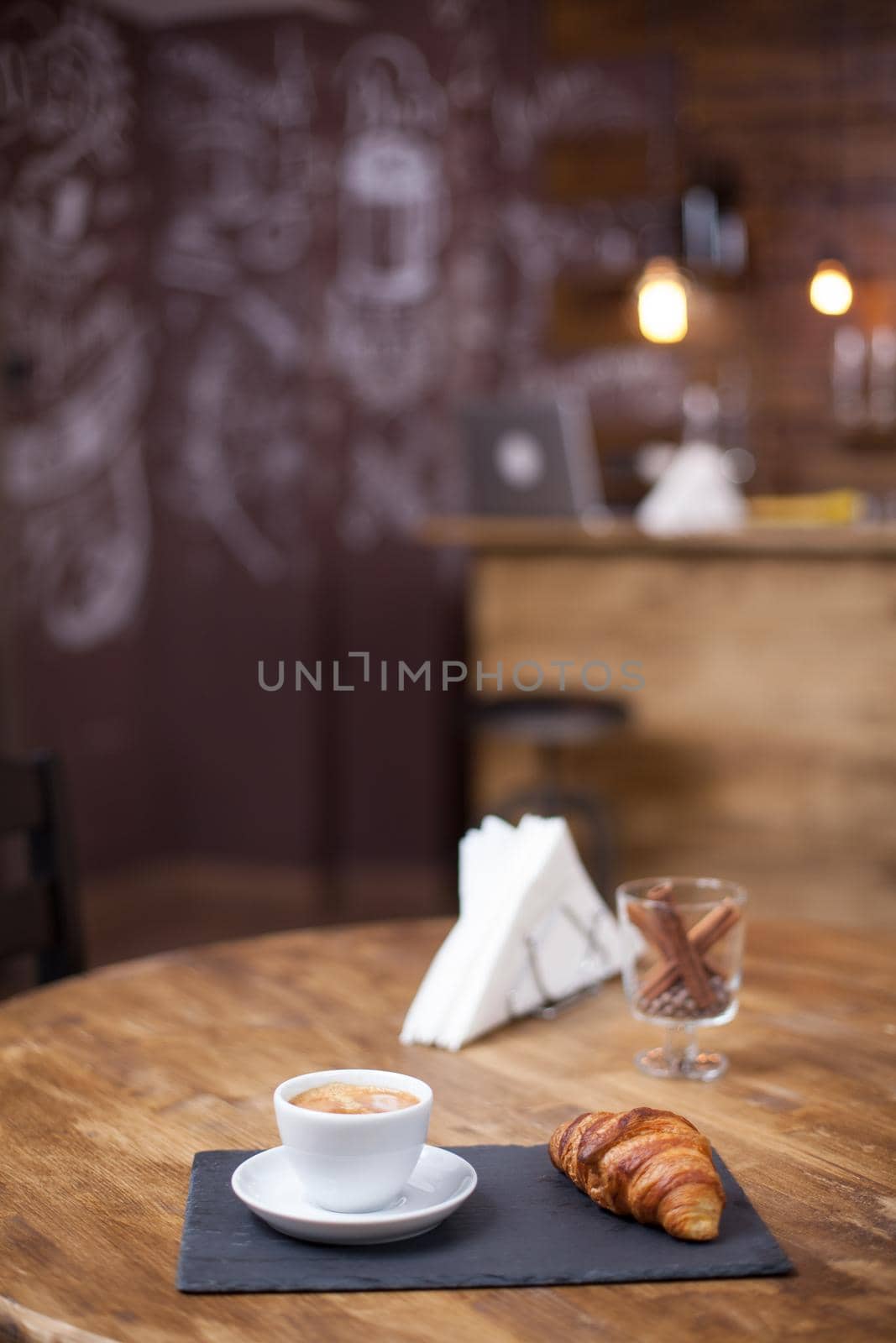 Fresh tasty espresso cup of hot coffee on a wooden next to a delicious croissant. Coffee shop design.